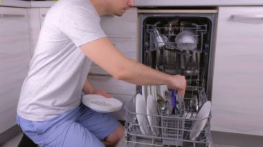 Tanınmayan adam bulaşık makinesine beyaz kirli tabaklar koyup mutfakta çalıştırıyor..