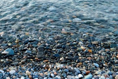 Küçük çakıl taşları olan taş çakıl taşı plajı ve sakin deniz saydam su yüzeyi. Doğa inanılmaz güzel deniz manzarası. Sahilde dinlenme yeri. Küçük okyanus dalgaları kıyıları eziyor.