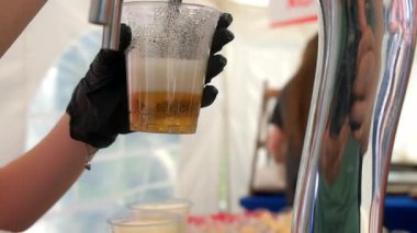 Barmen, sokak kafesindeki plastik bardaktan taze altın alkollü bira dolduruyor. Bir barda ya da açık hava etkinliğinde ferahlatıcı bir içecek sunma sürecini gösteriyor. Köpük kabı doldurur gibi köpürür..