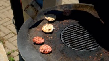 Caddedeki kafede spatulayla ızgarada köfte pişirmek, eller yakın plan. Açık havada fast food, yemek şirketi iş sektörü. Profesyonel aşçı eldiven giymiş. Etkinlik için mini burgerler hazırlıyor..