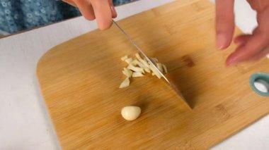 Aşçı kadın, ahşap tahtada ustalıkla sarımsak keserek yemek yapıyor. Taze malzemeler, mutfak teknikleri, ev yapımı sağlıklı sebzeler, yemek pişirme, keskin baharatlar..