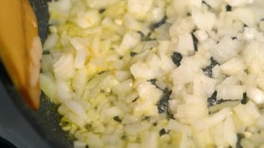 Yakın plan ahşap spatula, karıştırılmış soğan ve tavada sarımsak pişiriyor. Mutfak teknikleri, ev yapımı sağlıklı yemek hazırlama, yemek pişirme, mutfak, yemek tatma..