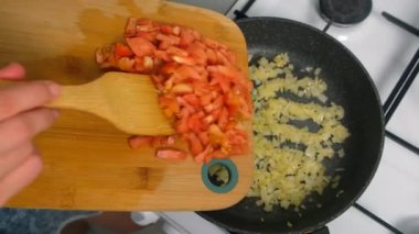 Aşçı kadın kızartma tavasına doğranmış domates ve kızarmış soğan ekliyor. Mutfak teknikleri, ev yapımı sağlıklı yemek hazırlama, yemek pişirme, yemek pişirme, baharat ve lezzetli yemekler..