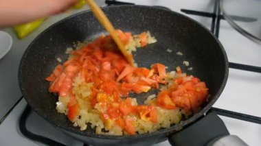 Aşçı kadın doğranmış domatesleri kızartılmış soğanla karıştırıyor. Mutfak teknikleri, ev yapımı sağlıklı yemek hazırlama, yemek yemeği, mutfak, yemek için baharat iyi tat..