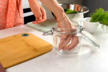 Salatalık turşusu pişirmek için cam kavanoz hazırlayan kadın evdeki mutfağa sarımsak koyuyor. Mutfak, aşçılık, yemek, ev yemeği, yemek tarifi, malzeme konsepti.