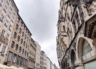 A view up at the various architectural styles of different eras of buildings in the historical part of Munich while walking along quiet, cozy streets on a cloudy rainy summer day.