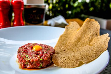 Bıldırcın yumurta ve ekmek cips yalanlarıyla beyaz tabakta klasik biftek tartar.