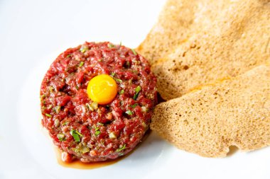 Bıldırcın yumurta ve ekmek cips yalanlarıyla beyaz tabakta klasik biftek tartar.