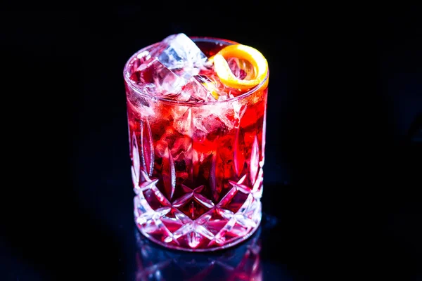 Red cocktail with ice, apparently, of Campari with red grapefruit on a black background.