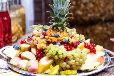 Dilimlenmiş meyve ve çilek (ananas, üzüm, elma, muz, ahududu, yaban mersini ve diğerleri) bir tabak slayt üzerinde yalan.