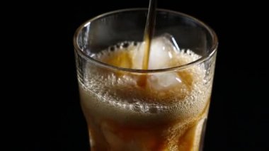 Cola kabarcıkları ile buz cam içine dökülür. Siyah arka plan