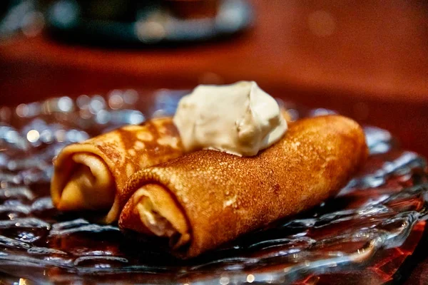 Pancakes rolled into a roll with sour cream lie on a plate