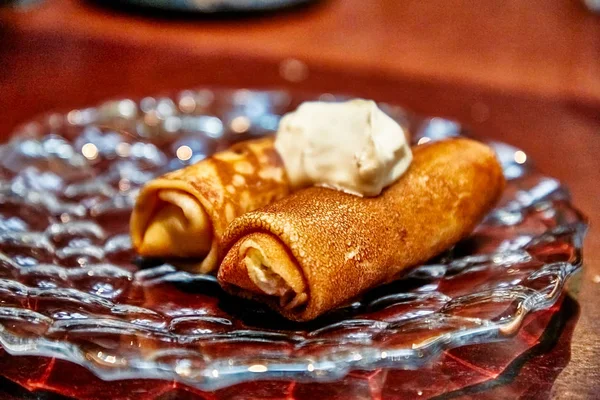 Pfannkuchen zu einer Rolle gerollt mit saurer Sahne liegen auf einem Teller — Stockfoto