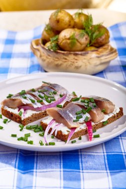 Sandviç balığı, kırmızı soğan, peynir ve patates tabakta.