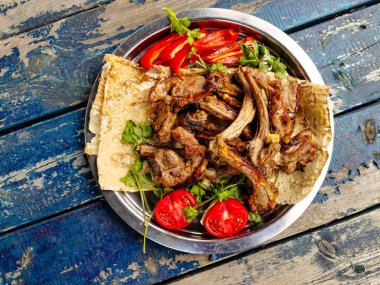 Izgara kuzu fileto, domates ve otlar tabakta.