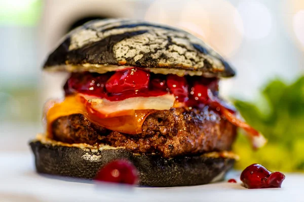 A black Burger with bacon and berry sauce is on the table.