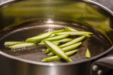 Şef kızartma tavasında ince dilimler halinde dilimlenmiş kabak kızartıyor.