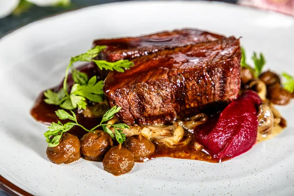 Grilled beef with mushrooms, mashed potatoes and beetroot sauce is on the plate
