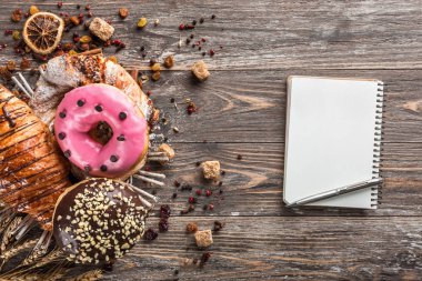 Fırından yeni çıkmış kruvasan, cracknel ve Not defteri ile ahşap masa üstünde kremalı bisküvi kahvaltıda, üstten görünüm