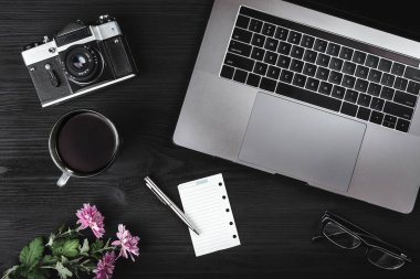 Ofis Resepsiyon çalışma alanı. Fincan çay veya kahve, fotoğraf makinesi, dizüstü bilgisayar, gözlük ve eski ahşap masa üzerinde yeşil pembe bitki. Üstten görünüm, düz yatıyordu