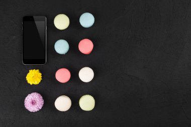 Üstten görünüm, düz yatıyordu. Boş ekran telefon mockup macarons ve çiçeklerle siyah arka plan üzerine. Metin alanı