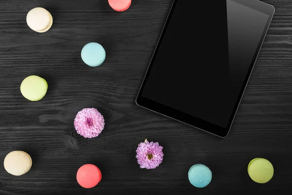 Digital tablet computer on old wooden background with macarons and pink flowers. Top view, flat lay