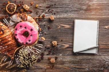 Fırından yeni çıkmış kruvasan, cracknel ve çörek sepeti Not defteri, üstten görünüm ile ahşap masa üzerinde krema ile