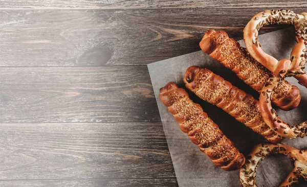 Top view, sausages in bread with sesame seeds and pretzels with sunflower seeds. Strong light is applied in the old wooden background