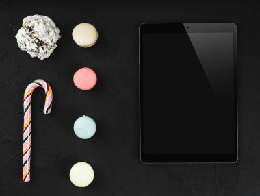 Yüksek çözünürlüklü renkli macarons, tatlı lolipop ve bisküvi taş siyah arka plan üzerine tablet. Kopya alanı, üstten görünüm