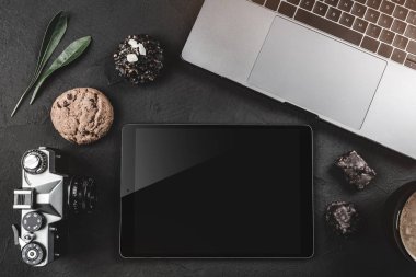 Siyah bir taş masanın üzerine çalışma, bir fotoğraf makinesi, bir grafik tablet ve tatlılar için bir dizüstü bilgisayar var. Üstten görünüm, düz yatıyordu