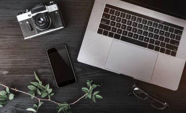 Çalışma alanı ile dizüstü bilgisayar, telefon, fotoğraf makinesi ve ahşap doku tablo gözlük. Üstten görünüm, düz yatıyordu stili