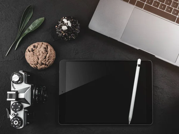 Dizüstü bilgisayar, dijital tablet ve fotoğraf makinesi, siyah bir masaüstü üstten görünüm. Kahve molası tatlılar, üstten görünüm