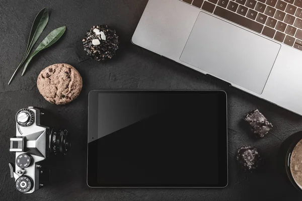 Siyah bir taş masanın üzerine çalışma, bir fotoğraf makinesi, bir grafik tablet ve tatlılar için bir dizüstü bilgisayar var. Üstten görünüm, düz yatıyordu