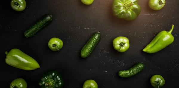 Various green vegetables on dark table. Top view, light effect