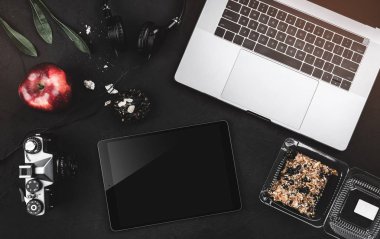 Açık laptop ile dijital tablet, tatlılar ve siyah taş masa üzerinde kırmızı elma. Üstten görünüm, düz yatıyordu stili