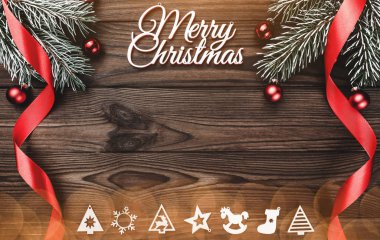 Bir Merry Christmas yazıt ve el yapımı ağaç oyuncak ve evergreen dalı kırmızı Küre ve ampuller ile ahşap arka plan üzerinde uzun kırmızı kurdele ile yukarıdan görüntülemek