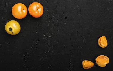 Sarı domates bütün, taze kesilmiş yarım veya çeyrek rustik siyah arka plan üzerine. Sonbahar sebze, üstten görünüm