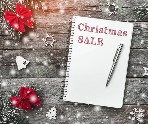 赤の弓と木製の灰色の背景に手作りおもちゃをクリスマスのモミの枝と本文書いて クリスマスのグリーティング カードのためのペンとメモ帳 雪と光の効果 — ストック写真