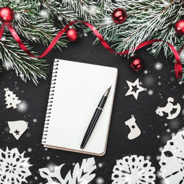 Çam dalları toplarla süslenmiş siyah taş zemin. Üstten görünüm, not defterinde metin için yer. Kar etkisi