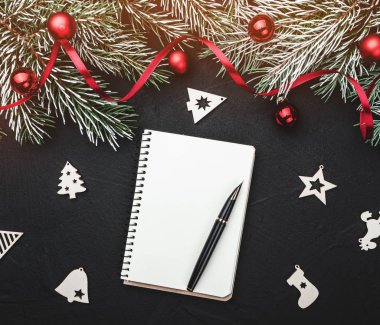 Kış kartı. Siyah taş arka plan. Topları ve kırmızı bolluk süslü çam dalları ile. Üstten görünüm. Not defterinde metin için yer. Işık efekti