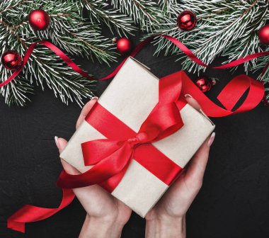 Kış kartı. Bir kızın elinde bir hediye elinde siyah bir taş zemin üzerine kırmızı bir bolluk ile tutun. Kırmızı topları ile süslü çam dalları ile. Üstten görünüm