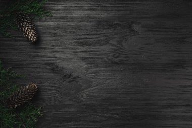 Noel kartı. Dalları ve çam kozalakları bir yan, üst görünümünde siyah ahşap zemin