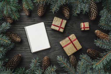 Noel kartı. Siyah ahşap zemin, çam dalları etrafında ve koniler. Noel Baba'nın mektubu. Altın hediye. Üstten görünüm