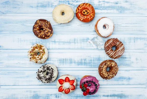 A circle of assorted donuts, on old wood background. Top view. Space for text.