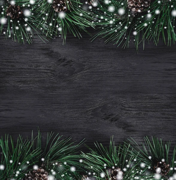 Christmas card. Black wood background with pine branches and pine cones from the top, top view. Xmas square card. Snow effect.