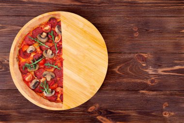 Baharatlı salam, roka, vişneli domates, mantar ve Teksas baharatlı pizzanın yarısı ahşap ahşap bir tabakta, üst görünüm ve kopyalama alanı.