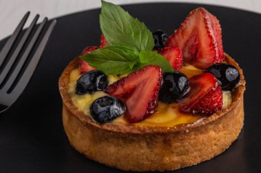 Lezzetli meyveli pasta ya da taze çilekli tart, kızılcık ve nane yaprağı siyah bir tabakta ve yanında bir çatal, yakın görüş