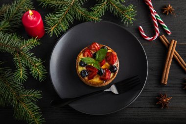Noel meyveli tart ya da böğürtlenli kek ve siyah desenli ahşap kaplı siyah tabakta nane. Köknar dalları, tarçın, yıldız anason, kırmızı mum ve şeker içeren Xmas kompozisyonu
