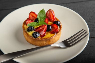 Meyveli kek, vanilyalı krema ve nane yaprakları beyaz tabakta çatalla, yakın görüş.