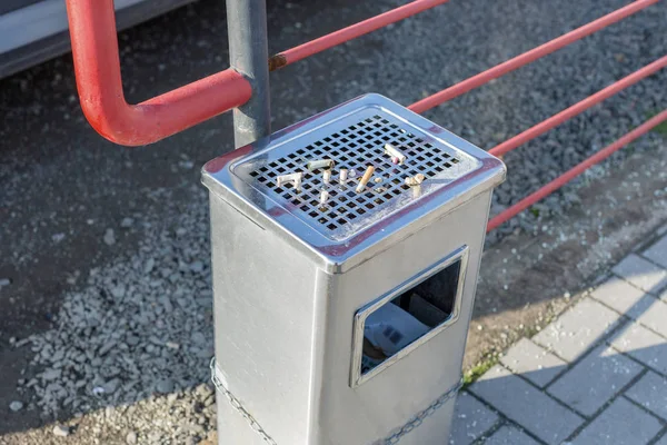 Street trash can with ashtray and cigarette butts. Trash can tied to the fence. Horizontal photo